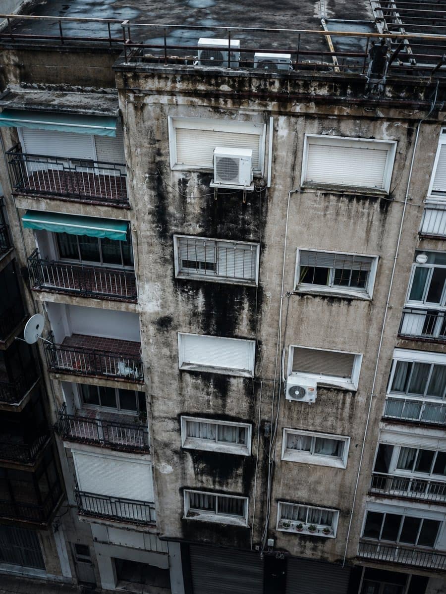 Fachada de un edificio de viviendas con humedad generalizada, manchas de moho y revestimiento degradado, vista desde el aire