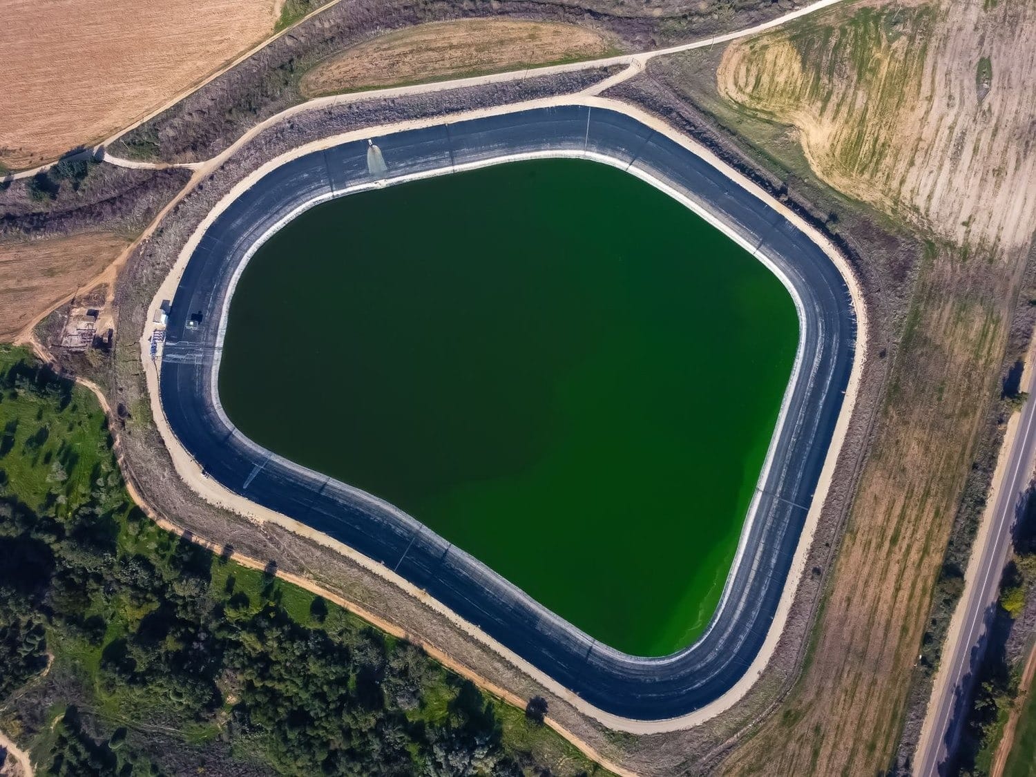 Vista aérea cenital de una balsa de riego impermeabilizada con lámina, en entorno agrícola